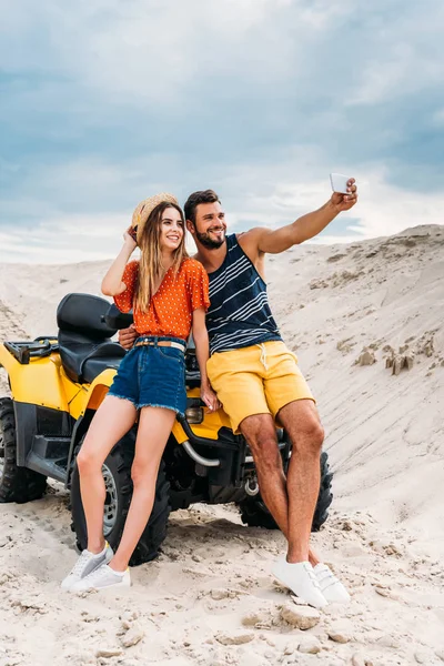 Sorrindo jovem casal com ATV tomando selfie no deserto — Fotografia de Stock