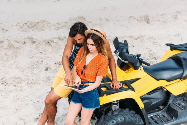 Vue grand angle de jeune couple avec VTT en utilisant une tablette numérique dans le désert — Photo de stock