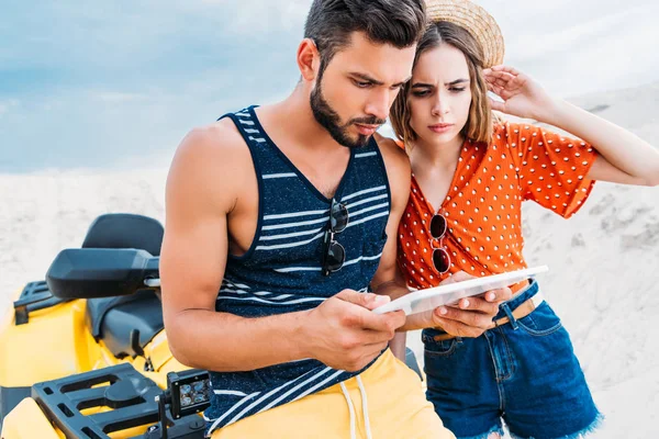 Confundido perdido joven pareja con ATV usando tableta digital en el desierto - foto de stock