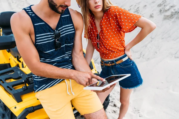 Corte tiro de jovem casal com ATV usando tablet digital no deserto — Fotografia de Stock