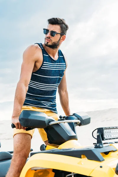 Handsome young man standing on all-terrain vehicle and looking away — Stock Photo
