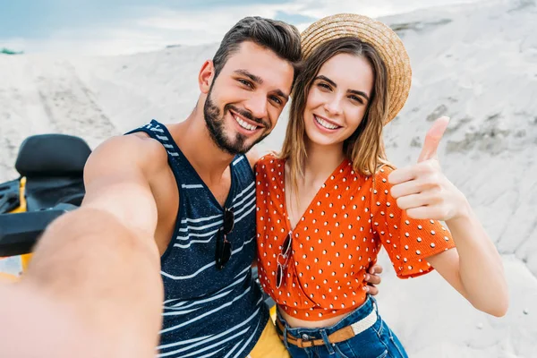 Punto de vista de la toma de una joven pareja tomando selfie y mostrando el pulgar hacia arriba en el desierto - foto de stock