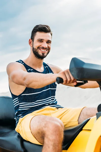 Joven feliz en vehículo todo terreno mirando a la cámara delante del cielo nublado - foto de stock