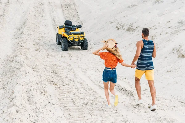 Visão traseira do jovem casal indo para ATV por duna arenosa — Fotografia de Stock