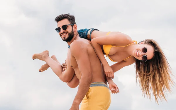 Happy young man carrying his girlfriend on shoulder and looking at camera — Stock Photo