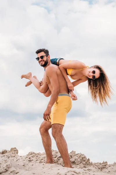 Handsome young man carrying his girlfriend on shoulder and looking at camera — Stock Photo