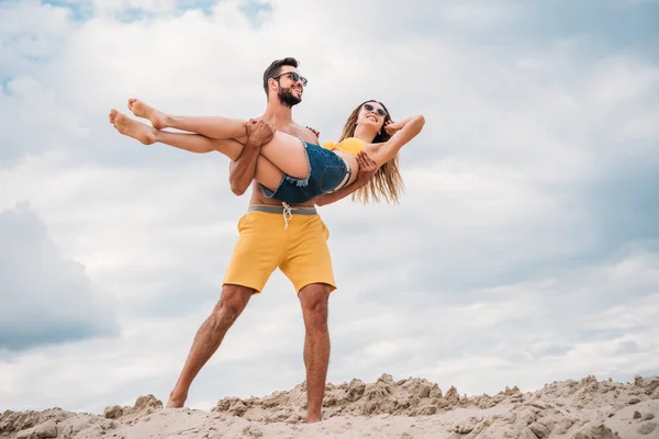 Schöner junger Mann, der seine Freundin trägt und an einer Sanddüne spaziert — Stockfoto