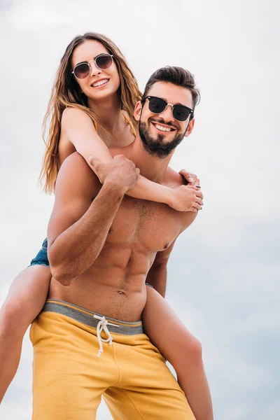 Feliz joven mujer piggybacking en novios de nuevo en frente de cielo nublado - foto de stock