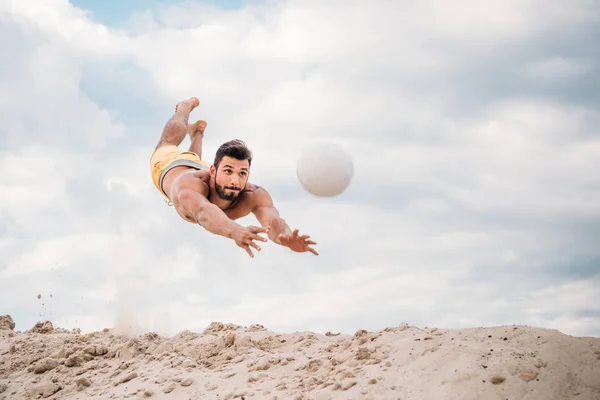 Jovem bonito pulando para bola enquanto joga vôlei de praia — Fotografia de Stock
