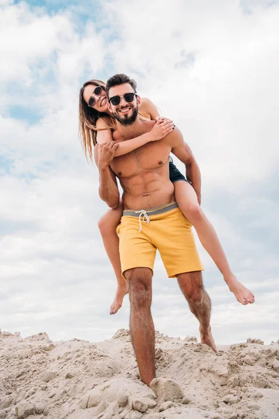 Attractive young woman piggybacking on boyfriends back at beach — Stock Photo