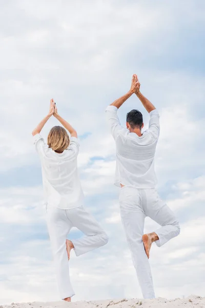 Rückansicht eines Paares, das Yoga in Baumpose (vrksasana) auf einer Sanddüne praktiziert — Stockfoto