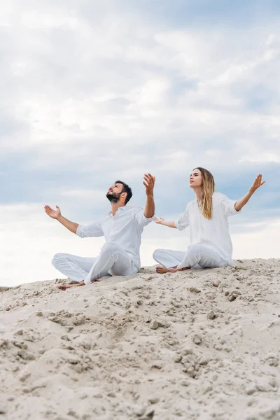 Young fit couple on yogi meditating while sitting on sandy dune in lotus pose (padmasana) — Stock Photo