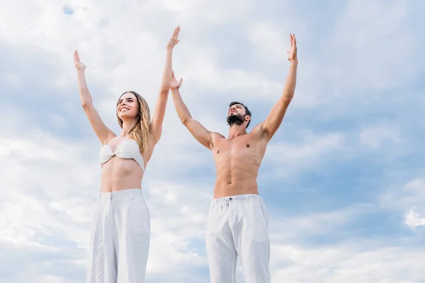 Подходит молодая пара с поднятыми руками, медитирующая под облачным небом — стоковое фото