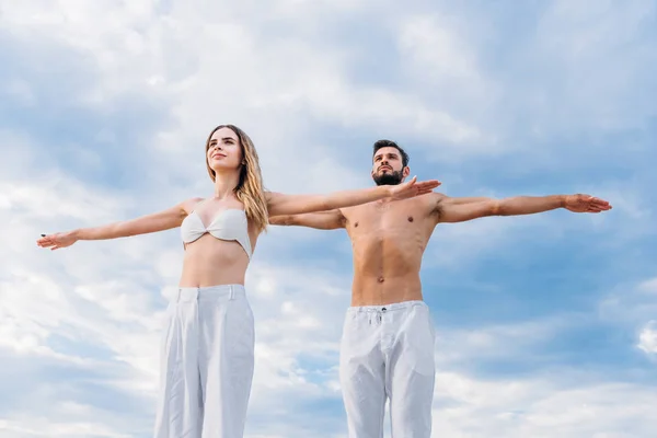 Sporty young couple with outstretched arms meditating under cloudy sky — Stock Photo