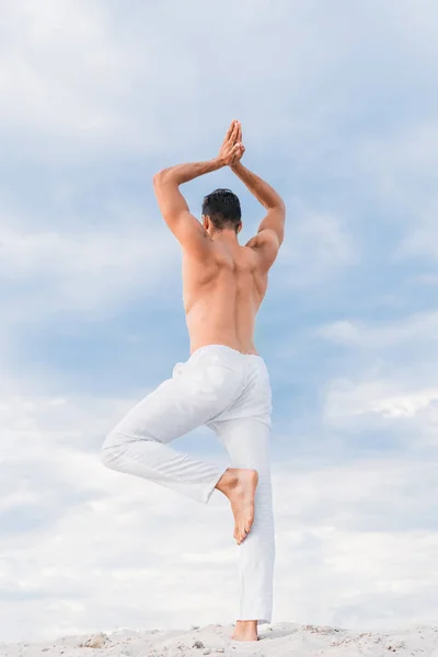 Beau jeune homme pratiquant le yoga en pose d'arbre devant le ciel nuageux — Photo de stock