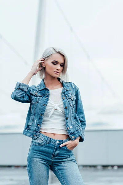 Beautiful young woman with bleached hair and in denim jacket on street — Stock Photo