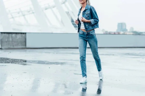 Cropped shot of young woman in denim jacket and jeans running by street — Stock Photo