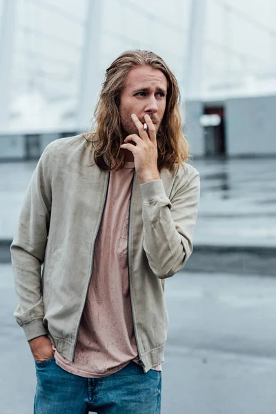Atractivo joven fumando cigarrillo en la calle en día nublado - foto de stock