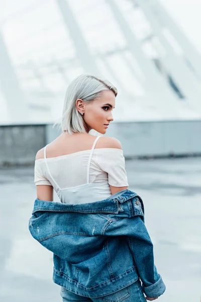 Vista posteriore di elegante giovane donna con i capelli sbiancati e in giacca di jeans sulla strada — Foto stock