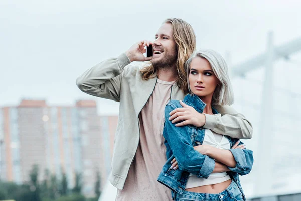 Glücklicher junger Mann umarmt seine Freundin und telefoniert — Stockfoto