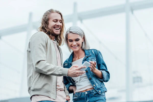 Feliz pareja joven utilizando el teléfono inteligente juntos en la calle - foto de stock