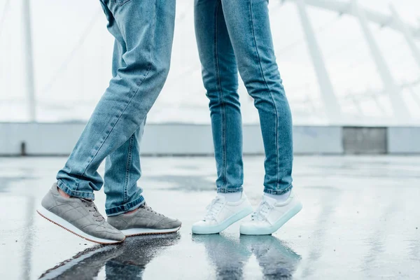 Cropped shot of couple in jeans and sneakers flirting on parking — Stock Photo