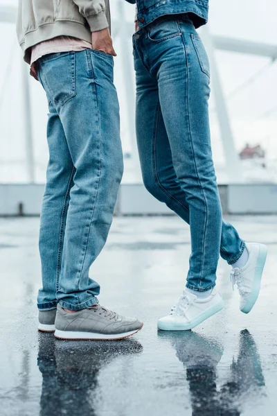 Recortado disparo de joven pareja en jeans y zapatillas de deporte coqueteando en el aparcamiento - foto de stock