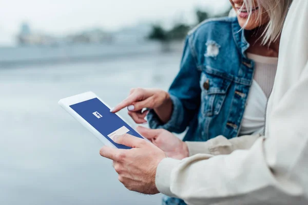 Colpo ritagliato di giovane coppia utilizzando tablet con applicazione facebook sullo schermo insieme — Foto stock