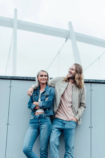 Belo jovem casal inclinando-se para trás na parede e olhando para longe — Fotografia de Stock