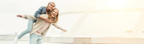 Tiro panorâmico de feliz jovem mulher piggybacking em namorados de volta — Fotografia de Stock