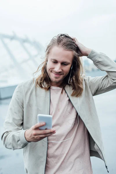 Glücklicher junger Mann hört Musik mit Kopfhörern und Smartphone auf der Straße — Stockfoto