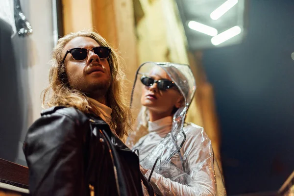 Jovem casal atraente em roupas elegantes olhando para longe na rua à noite — Fotografia de Stock