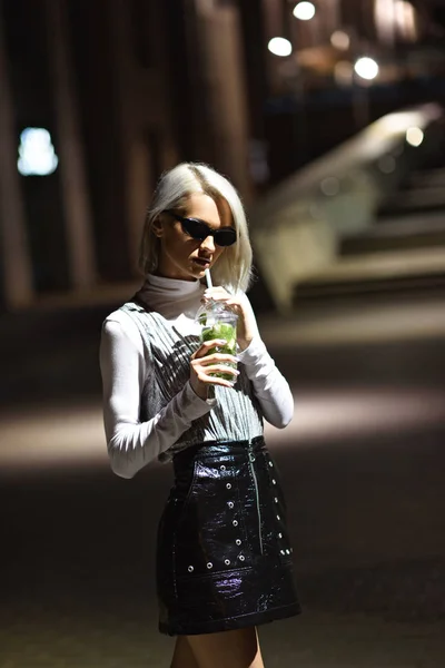 Beautiful young woman with mojito in plastic cup on dark street — Stock Photo