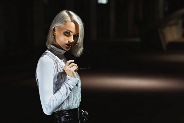 Mujer joven mirando a la cámara en la calle por la noche bajo la luz de la linterna - foto de stock