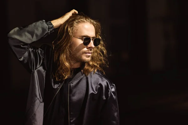 Attractive young man in sunglasses and leather jacket on street at night — Stock Photo