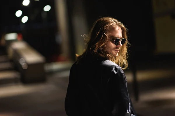 Jovem elegante em óculos de sol e jaqueta de couro na rua à noite — Fotografia de Stock