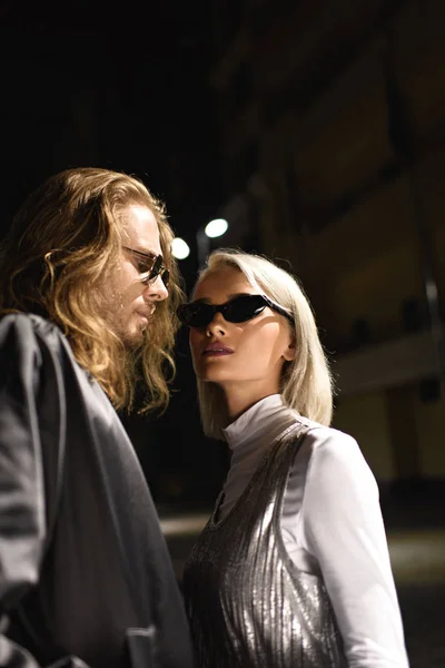 Joven pareja de moda en gafas de sol coqueteando en la calle por la noche - foto de stock