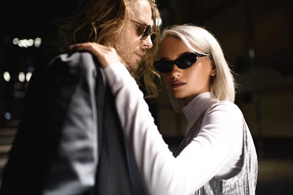 Joven elegante pareja en gafas de sol abrazando en la calle por la noche - foto de stock