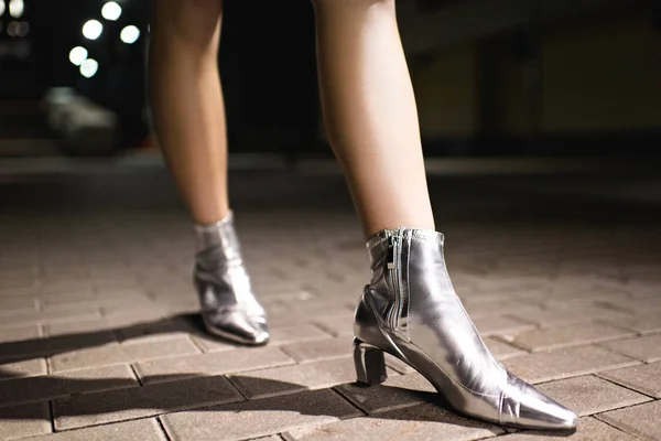 Tiro cortado de mulher em botas de prata brilhante andando na rua à noite — Fotografia de Stock