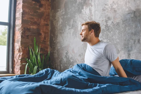 Bel giovane uomo svegliarsi nel suo letto durante il mattino a casa — Foto stock