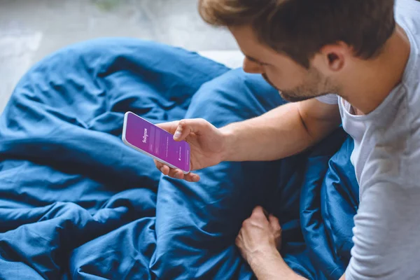 Избирательный фокус молодого человека в постели с помощью смартфона с Instagram на экране — стоковое фото