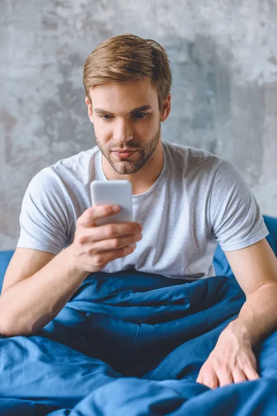 Junger Mann benutzt Smartphone zu Hause im Bett — Stockfoto