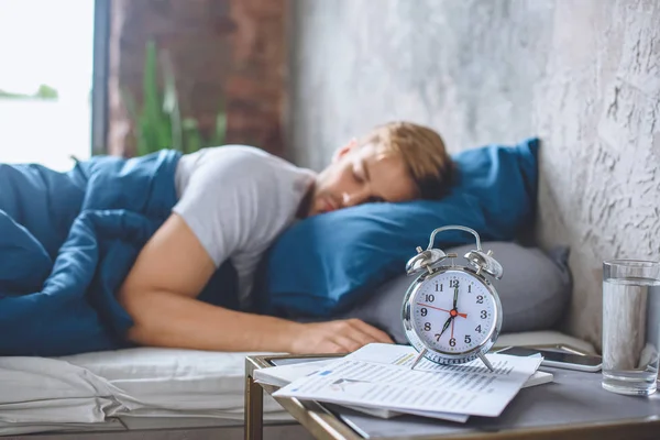 Selective focus of alarm clock and sleeping man in bed behind — Stock Photo