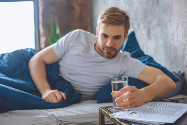 Selektiver Fokus junger Mann im Bett, der zu Hause ein Glas Wasser trinkt — Stockfoto