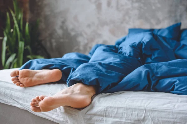 Imagen recortada de dormir mens piernas bajo manta en la cama en casa - foto de stock