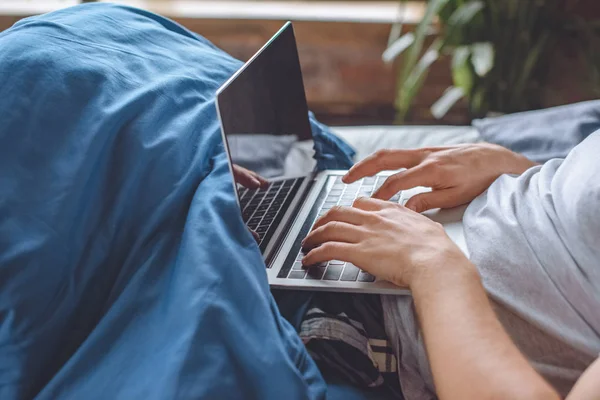 Imagen recortada del hombre en la cama con el ordenador portátil con pantalla en blanco - foto de stock