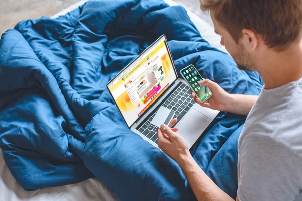 Hombre con tarjeta de crédito e iphone haciendo compras en línea en el ordenador portátil con aliexpress en la pantalla - foto de stock