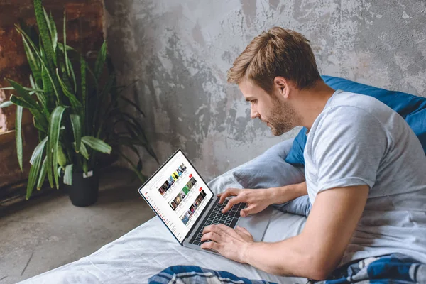 Joven guapo en la cama usando el ordenador portátil con youtube en la pantalla - foto de stock