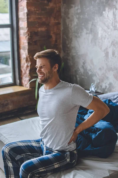 Young man with pain in spine just wake up and sitting on bed — Stock Photo