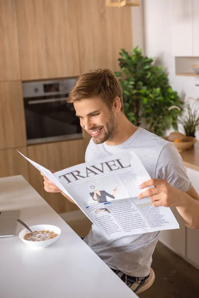 Улыбающийся мужчина читает газету за кухонным столом с завтраком — стоковое фото